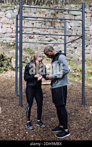 Full length of male and female athletes using technologies by monkey bars in forest Stock Photo