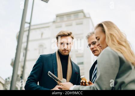 Low angle view of worried business executives looking at mobile phone while standing in city Stock Photo