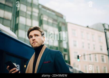 Low angle view of businessman looking away while standing against bus in city Stock Photo