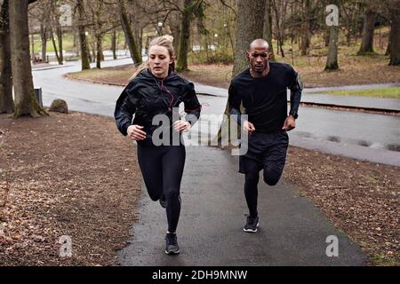 Full length of multi-ethnic couple jogging on wet street Stock Photo