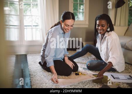 Smiling female designers discussing while sitting on carpet at home office Stock Photo
