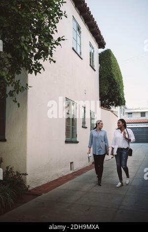 Full length of female designers discussing while walking on sidewalk by building against sky Stock Photo