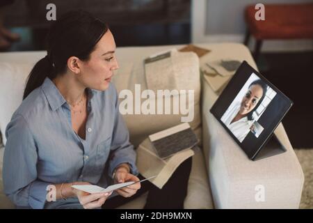 Architect with fabric swatch talking through laptop on video conference while working at home Stock Photo