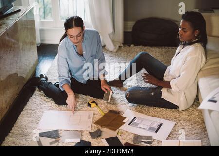 High angle view of female designers discussing about fabric swatch while sitting on carpet at home office Stock Photo