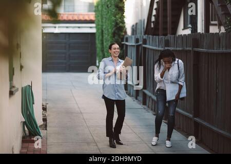 Female designers discussing while walking on sidewalk by building against sky Stock Photo