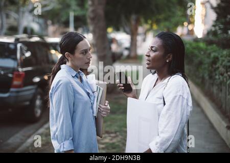 Side view of architect discussing with colleague while standing on footpath Stock Photo