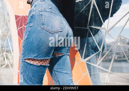 Midsection of young woman wearing torn jeans against mosaic wallMidsection of young woman wearing torn jeans against mos Stock Photo