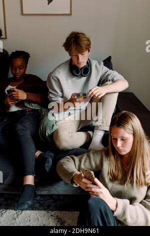 Teenage girls and boy using mobile phone while sitting in living room Stock Photo