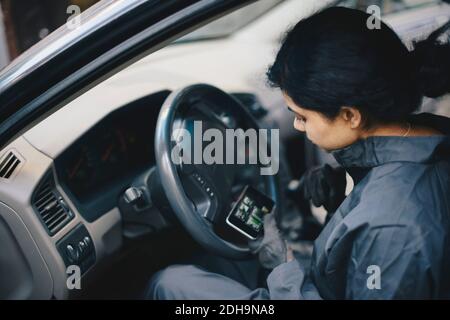 Female mechanic using mobile phone while sitting in car Stock Photo