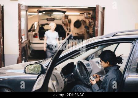 Side view of female mechanic using mobile phone while sitting in car Stock Photo