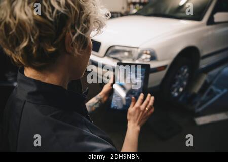 Female mechanic using digital tablet by car in auto repair shop Stock Photo