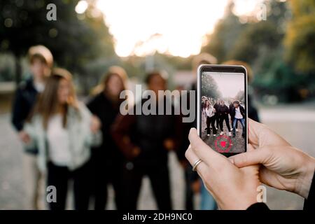 Cropped hands of woman with smart phone filming teenagers dancing on street in city Stock Photo
