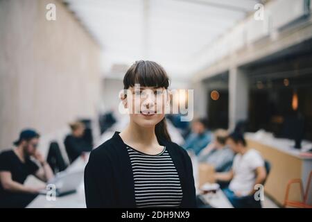 Portrait of female confident computer programmer at office with colleagues working in background Stock Photo
