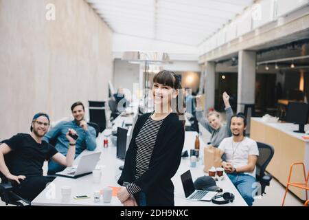 Portrait of happy female computer programmer with colleagues sitting at desk in background Stock Photo