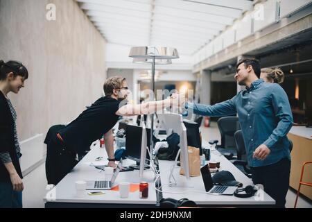 Male computer programmers holding hands over desk in office Stock Photo