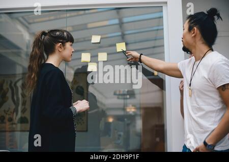 Male programmer explaining adhesive note to female colleague in office Stock Photo