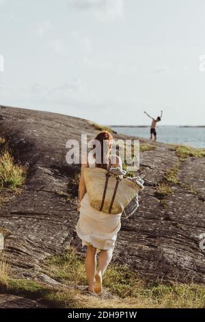 Rear view of woman with bag walking on land against sky during sunny day Stock Photo