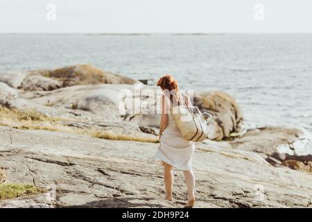 Rear view of woman with bag walking against sky during sunny day Stock Photo