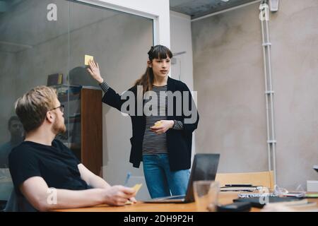 Female computer programmer showing adhesive note while giving presentation to colleague in office Stock Photo