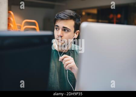 Thoughtful computer programmer wearing in-ear headphones in office Stock Photo