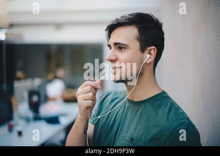 Young male computer programmer using in-ear headphones while talking in office Stock Photo