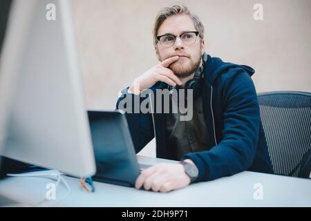 Thoughtful computer programmer sitting at desk in office Stock Photo