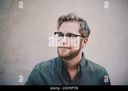Thoughtful male computer programmer looking away against beige wall in office Stock Photo