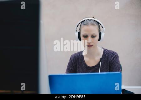 Female computer programmer wearing headphones while using laptop in office Stock Photo