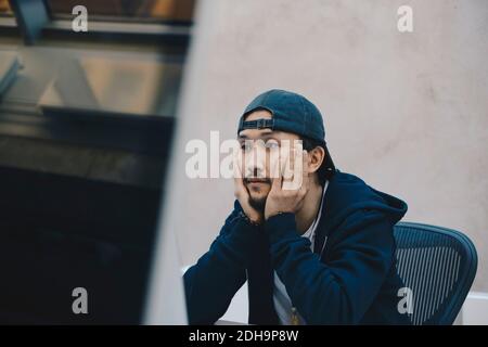 Young computer programmer using computer while sitting with head in hands at office Stock Photo