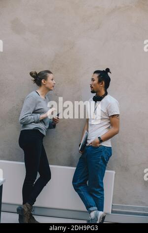Male and female computer programmers discussing while leaning on wall in office Stock Photo