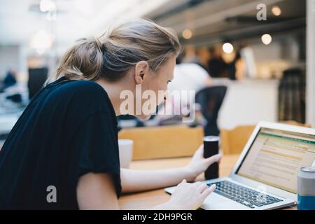 Side view of young female computer programmer using laptop at desk in office Stock Photo