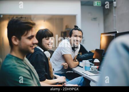 Happy male and female computer programmers talking at desk in office Stock Photo
