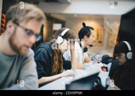 Female programmer working on computer with male colleagues at desk in office Stock Photo