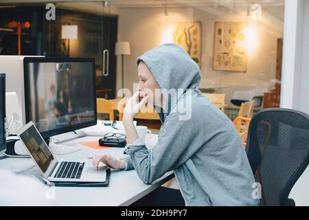 Side view of computer programmer using laptop at desk in office Stock Photo