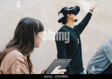 Male computer programmer gesturing while using VR glasses by colleagues in office Stock Photo