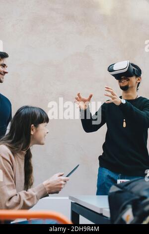 Smiling male computer programmer gesturing while using VR glasses by colleagues in office Stock Photo