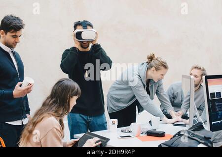 Male computer programmer using VR glasses while colleagues working in office Stock Photo