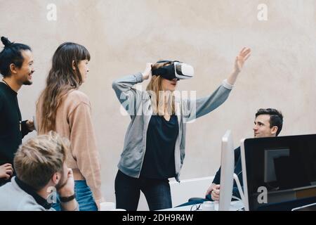 Female computer programmer using VR glasses while standing with colleagues in office Stock Photo