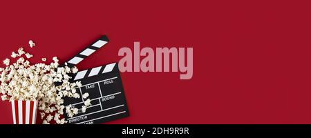 Watching movie with popcorn and clapperboard on red background. Movie goers accessories, cinematography concept. Long wide banner with copy space Stock Photo