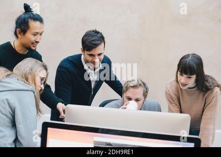 Male computer programmer drinking coffee while using computer with colleagues in office Stock Photo