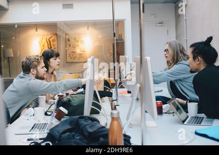 Female computer programmer showing digital tablet to colleagues at desk in office Stock Photo