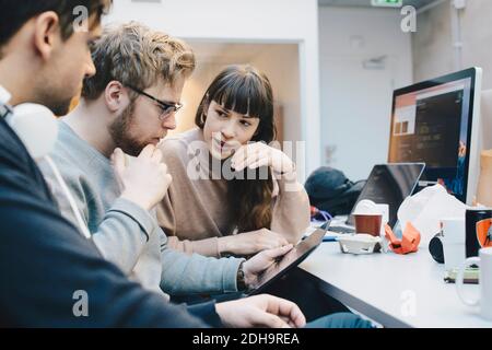 Male and female computer programmers discussing over digital tablet at desk in office Stock Photo