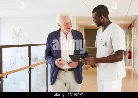 Male nurse and senior male patient discussing over digital tablet at hospital corridor Stock Photo