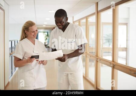 Happy male and female nurse using digital tablet while examining document in hospital corridor Stock Photo