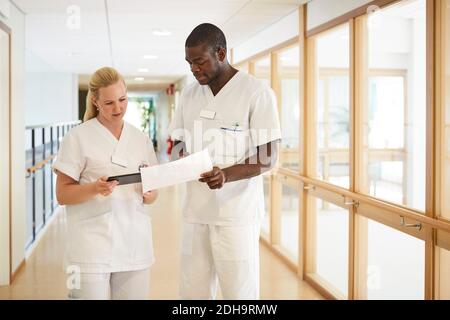 Male and female nurse using digital tablet while examining document in hospital corridor Stock Photo