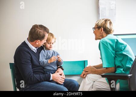 Side view of mature female doctor talking to boy with father in clinic Stock Photo