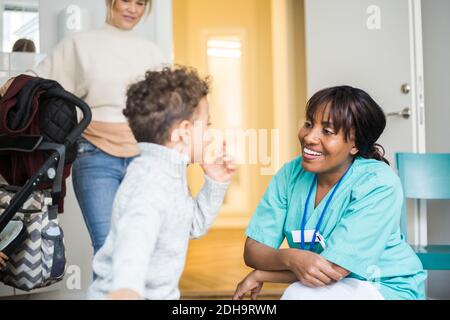 Boy talking to smiling female nurse while mother standing in background at medical clinic Stock Photo