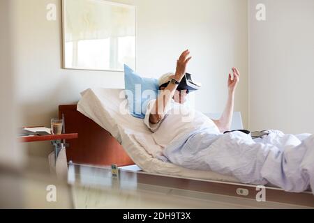 Senior man using VR glasses on bed in hospital ward Stock Photo