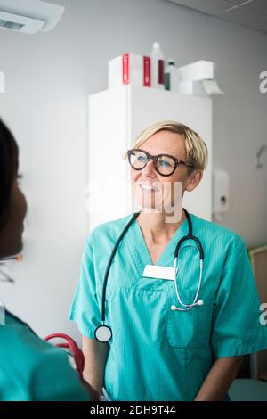 Smiling mature pediatrician talking to female healthcare worker in clinic Stock Photo