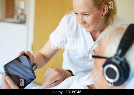 Smiling female nurse using digital tablet with senior man in hospital ward Stock Photo